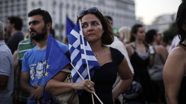 A protestor holds a European Union and Greek flag during a pro-European Union (EU) rally at Syntagma Square in Athens, Greece, on Thursday, July 9, 2015. The government of Greek Prime Minister Alexis Tsipras drafted a new proposal it hopes will convince creditors to let the country stay in the euro. Photographer: Simon Dawson/Bloomberg