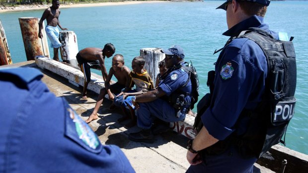 Young local Aboriginal kids play on the main wharf on Palm Island while Police officers from the Personal Safety Response Team PSRT patrol the island.