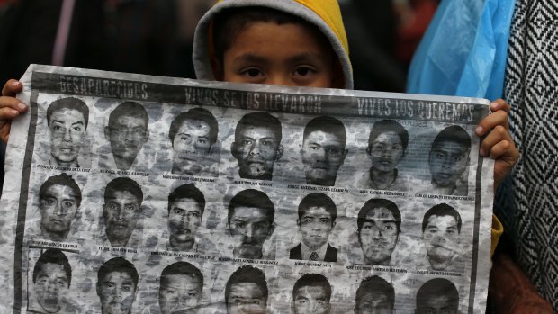 Dubious treatment: A boy holds up a sheet of photos showing some of the missing 43 students at the Independence monument in Mexico City.