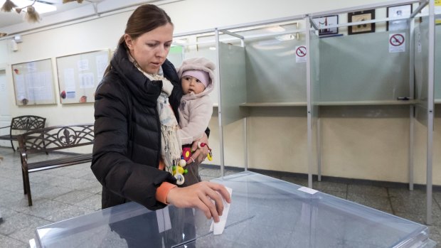 A woman holding a child casts her ballot at a polling station during parliamentary elections in Vilnius, Lithuania.