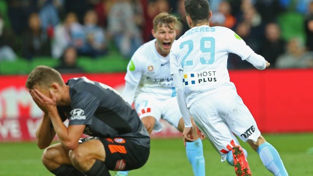 Anthony Caceres and Nick Fitzgerald of Melbourne City celebrate a goal as Daniel Bowles of the Roar looks dejectedat AAMI Park.