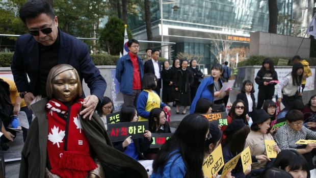 An activist puts his coat around the shoulders of the statue symbolising women and girls forced into sex slavery by the Japanese. The statue was placed outside the Japanese embassy in Seoul   in 2011.