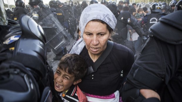 A woman and child flee as police respond with force against migrants protesting on the Serbia-Hungary border after they pushed through the border fence into Hungary.