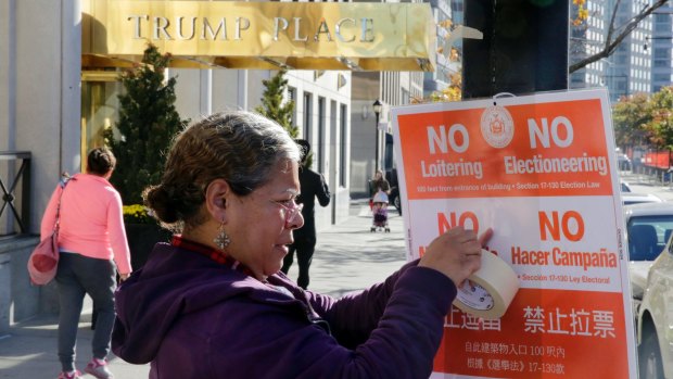 A woman attaches a sign outside a polling place in a  New York City apartment building named after Donald Trump.