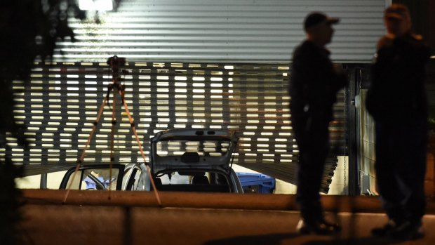 Officers examine the scene where a fire-damaged car rammed into a police roller door.