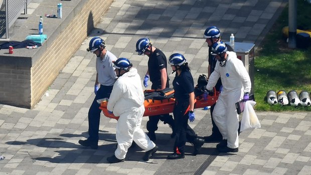 Police forensics carry a body bag on a stretcher out of the Grenfell Tower block.