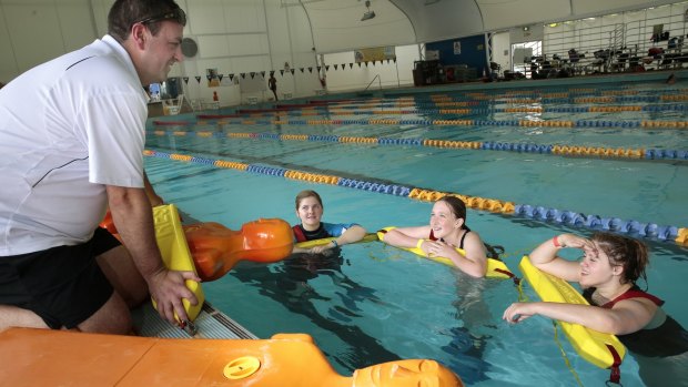 Royal Life Saving ACT training manager Ben Cuttriss instruct Calwell High School students Kirralee- Rose Schofield, year 10, Nia Cavanagh, year 7, and Lauren Smith, year 10, on the manikin tow during the school's swimming carnival at the Canberra Olympic Pool.