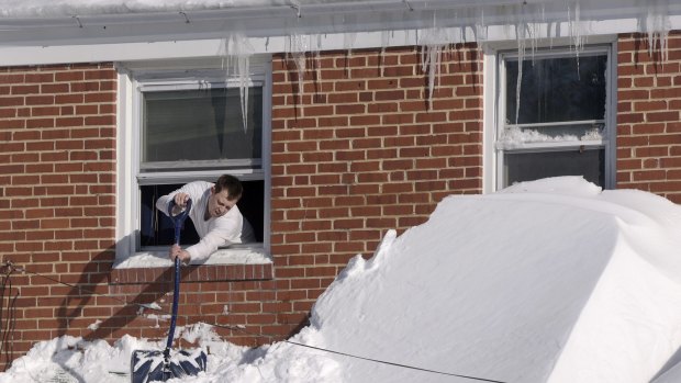 Shawn Covelly knocks snow off his awning, on Sunday in Towson, Maryland.