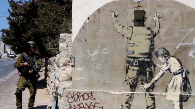 An Israeli soldier walks past by a Banksy graffitti in Bethlehem.