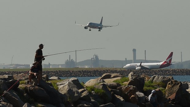 Two men fishing at Botany Bay as planes come into land and prepare to take off at Sydney Airport.