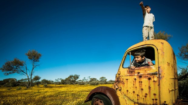Jai and Kaiden Lane play atop an abandoned vehicle amid a burst of WA wildflowers on old Lochada Station.