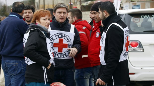 Aid workers stand near a convoy of vehicles loaded with food and other supplies organised by the International Committee of the Red Cross, the Syrian Arab Red Crescent and the UN, as it makes its way to Madaya.