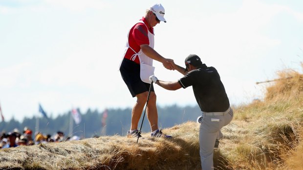 Jason Day climbs out of a bunker with help from his caddie.