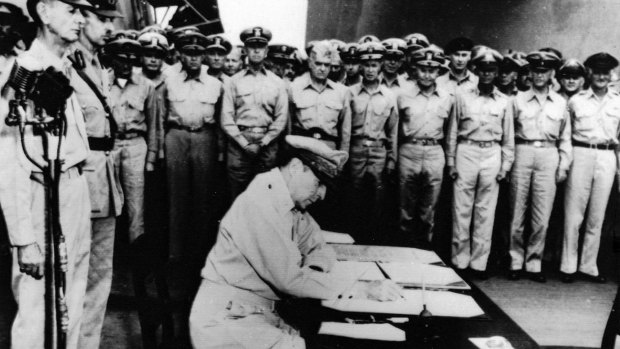General Douglas MacArthur signs during the formal surrender documents aboard the battleship USS Missouri. Directly behind him are the Lt. General Jonathan Wainwright, hero of Bataan and Corregidor, and Lt. Gen. A.E. Percival (R), British Commander who surrendered to Japan at Singapore.