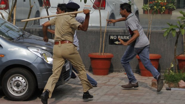 An Indian policeman chases protesters.
