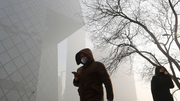 People wearing protection masks walk near the iconic headquarters of China's state broadcaster Central China Television in Beijing on Tuesday.