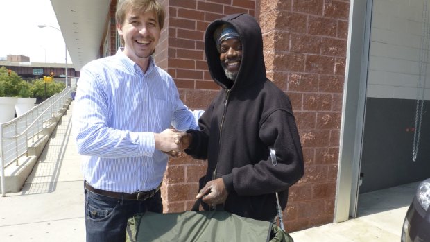 Tony Clark hands over a swag bed in a backpack to a homeless man.