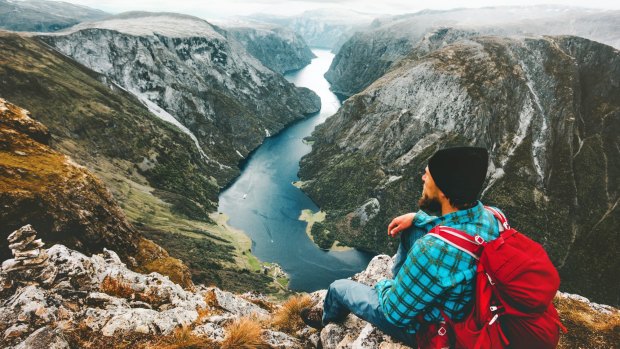Man with backpack relaxing on mountain summit traveling alone in Norway Lifestyle adventure vacations getaway above Naeroyfjord landscape aerial view SatFeb9cover - journeys - Ute Junker Credit: Shutterstock
