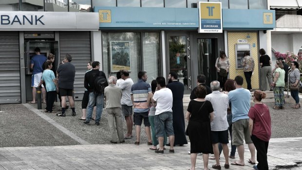People queue to use ATM machines to withdraw cash at a bank in Athens.