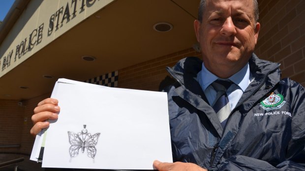 Detective Inspector Kevin McNeil with a copy of the butterfly pendant police hope will identify a woman found dead in Tathra on Wednesday.