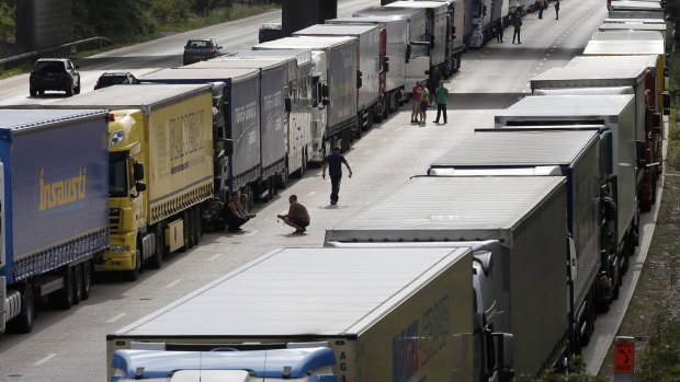 Drivers stand and sit next to their lorries awhich are backed up on the M20 motorway.
