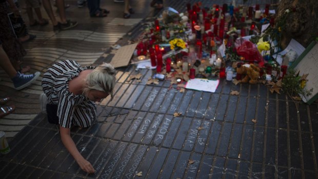 A woman writes a message on the ground at a tribute to those killed and wounded in the Barcelona atrocity.
