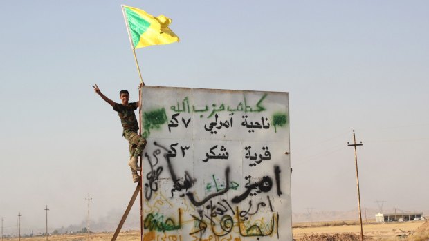 A member of Iraq's Hezbollah Brigades holds the Shiite militia's flag above a sign seven kilometres from the Iraqi town of Amerli in September, after Shiite militias helped break Islamic State's siege of the town.