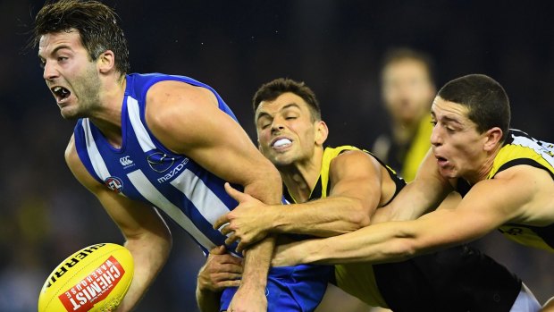 North Melbourne's Luke McDonald attempts to handball as Tigers Sam Lloyd and Jason Castagna apply pressure.