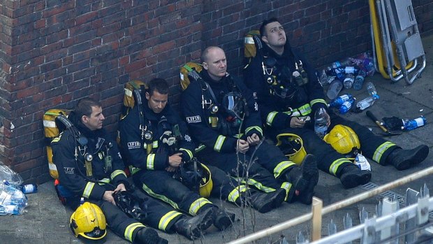 Exhausted firefighters, pictured resting on Wednesday morning, had to run to the building under riot shields held by police.