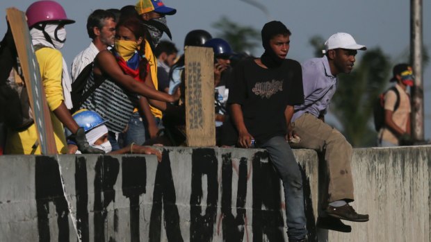 Anti-government protesters take positions behind a road wall covered with the Spanish word "Dictatorship" in Caracas.