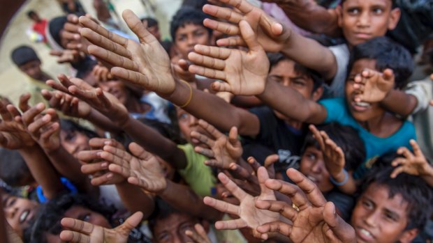 Rohingya Muslim children, who crossed over from Myanmar into Bangladesh, stretch their arms out to collect chocolates and milk distributed by Bangladeshi men at a refugee camp.