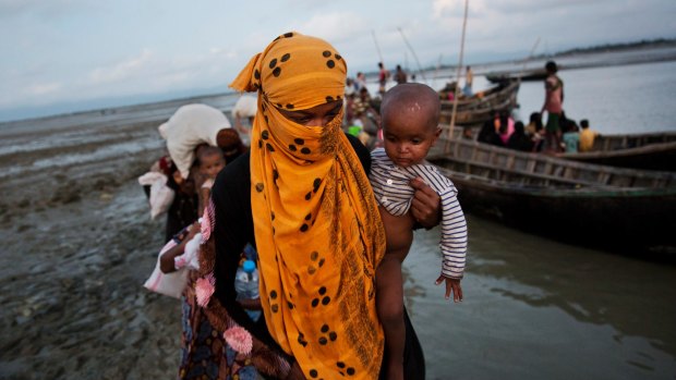 A Rohingya woman carries a child after crossing a stream on a small boat in Bangladesh after escaping violence in Myanmar.