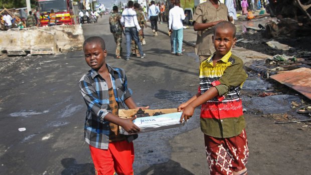 Somali children assist other civilians and security forces in their rescue efforts by carrying away unidentified charred human remains in a cardboard box, to clear the scene of the blast.
