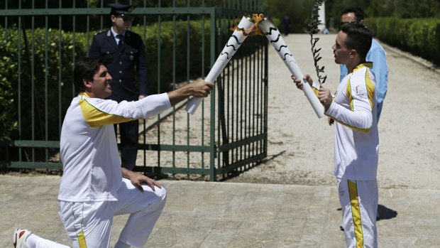 All yours: Former Brazilian volleyball player Giovane Gavio kneels as he receives the Olympic flame from Greek gymnast Eleftherios Petrounias.
