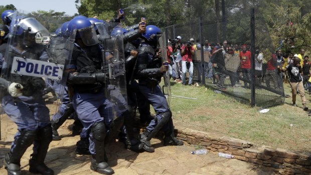 Riot police officers use pepper spray on students throwing stones. 