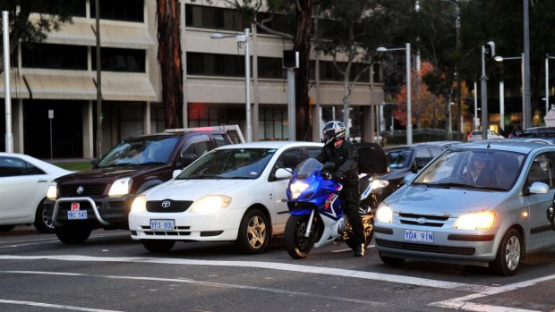 A motorcyclist waits at a red light between cars at the intersection of Northbourne Avenue and Barry Drive. 