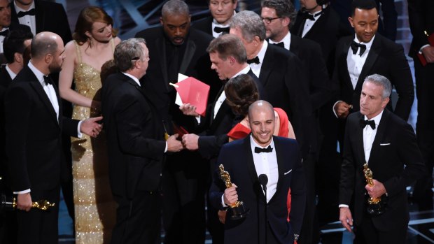 Fred Berger, producer of La La Land, foreground centre, gives his acceptance speech as members of PricewaterhouseCoopers, Brian Cullinan, holding red envelope, and Martha L. Ruiz, in red dress, and a stage manager discuss the best picture announcement error. 