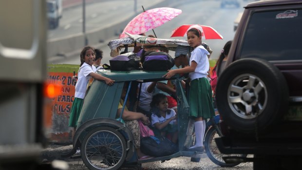 Filipino children dodge Manila's inappropriate public transport by hanging on to an overloaded tricycle on a busy road on their way to school on Monday.