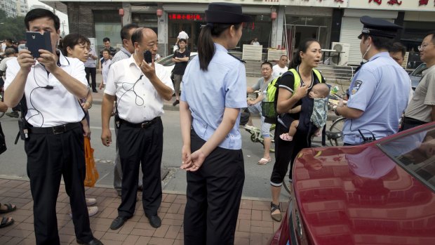 Yuan Shanshan, the wife of detained Chinese lawyer Xie Yanyi, carries her child as she talks to a police officer while other plain clothes security personnel film journalists near the Tianjin court on Tuesday.