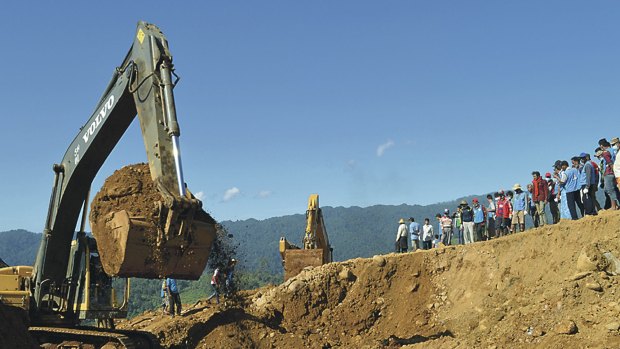 Excavators dig soil to search for bodies of miners as workers and rescue members gather in Hpakant, Kachin State, Myanmar.
