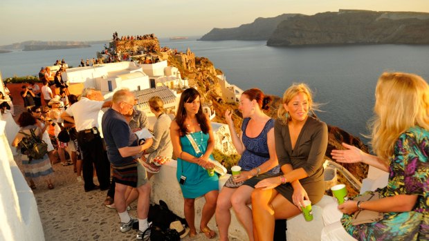 Tourists crowd walkways at Oia on Santorini as the sun sets.