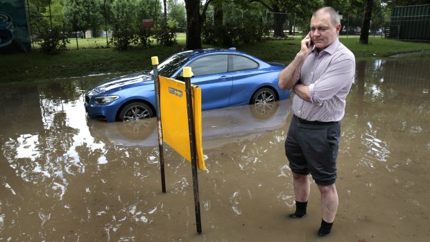 Michael Rorke on the phone to his insurance company after becoming stuck in a flooded part of the parking lot at Canberra Olympic Pool.
