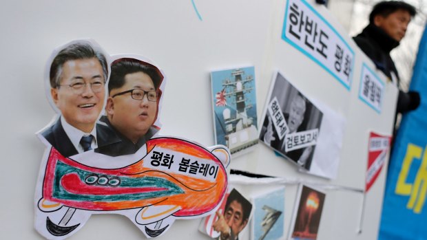 A South Korean protester holds a sign with pictures of President Moon Jae-in, left, and North Korean leader Kim Jong-un, second left, during a rally to denounce the US policy against North Korea and demand a peaceful Winter Olympics. 