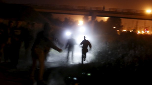 Fleeing migrants illuminated by police torches.