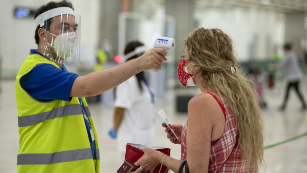 A passenger's temperature is checked at Madrid's airport. Even with a vaccine, travel is unlikely to return to how it was before the COVID-19 outbreak.
