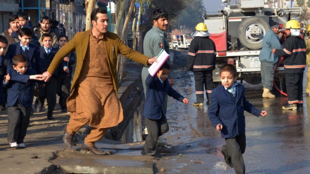 An Afghan teacher, in brown, helps school children run from the site of clashes near the Pakistan consulate in Jalalabad.
