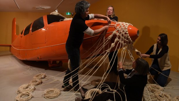Artists Claire Healy and Sean Cordeiro cover a light plane with macrame, with help from Susan Hutchison and Renael Carolin from the Aboriginal Women's Weaving Group.