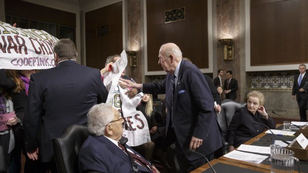 Former US secretary of state George Shultz stands to move protesters away from Henry Kissinger.