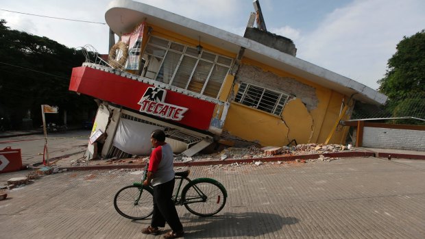 A man walks his bike past a building felled by a 7.1 earthquake, in Jojutla, Morelos state, Mexico.