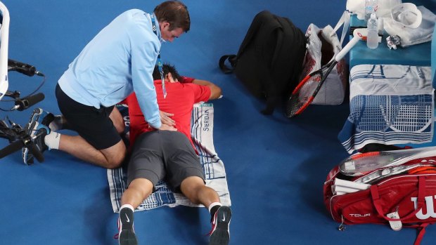 Kei Nishikori, laying down, is treated by a trainer during a break in play.